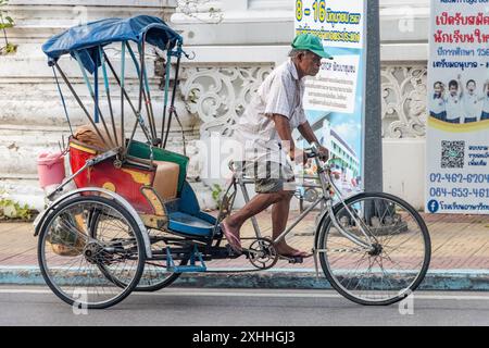 SAMUT PRAKAN, THAILANDIA, 16 GIUGNO 2024, Un uomo guida un triciclo per trasportare un passeggero in una strada della città Foto Stock