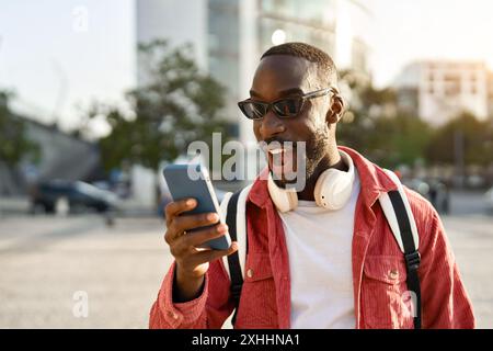 L'uomo africano stupito che si trova in strada a guardare il telefono si sente sorpreso. Foto Stock