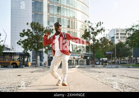 Felice giovane africano in cuffie che ballano per strada in città, corpo intero. Foto Stock
