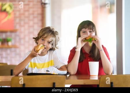 Bambini che mangiano fast food. Cibo spazzatura malsano. I bambini mangiano hamburger, patatine e pepite di pollo nel fast food. Bambino e ragazza che pranzano. Spuntino veloce Foto Stock