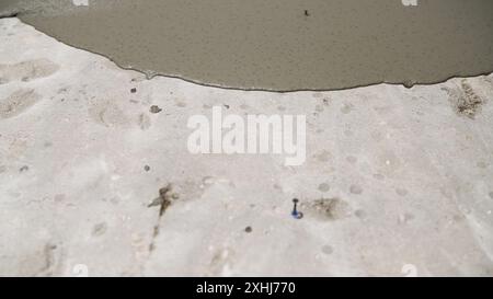 Il concetto di livellamento del pavimento con una miscela. I lavoratori versano la soluzione da un secchio sul pavimento in cemento. I lavoratori versano la miscela sul Foto Stock