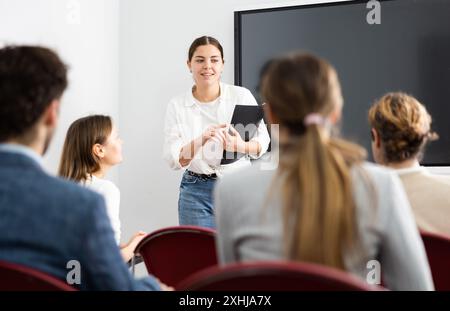 Ritratto di una giovane donna d'affari che si trova vicino al consiglio interattivo e partecipa a un seminario aziendale in auditorium Foto Stock