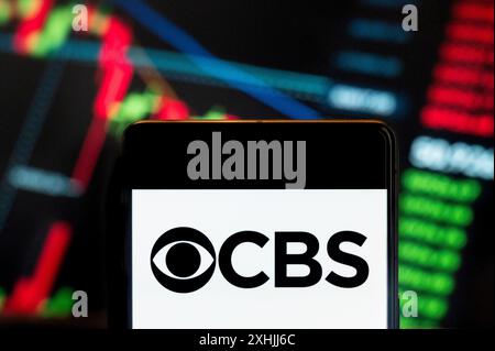 In questa illustrazione fotografica, il logo CBS della rete televisiva e radiofonica commerciale in lingua inglese americana visualizzato su uno smartphone con un grafico dell'indice di borsa economica sullo sfondo. Foto Stock