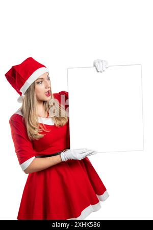 La giovane donna latina vestita da mamma Claus con un abito rosso ha sorpreso guardando un cartello con spazio di copia isolato su sfondo bianco Foto Stock