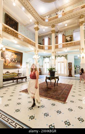 Le donne ospiti camminano intorno all'atrio della hall dorata dove persone famose socializzavano in passato, lo storico Menger Hotel, San Antonio, Texas, USA Foto Stock