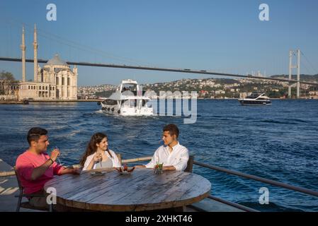 Turchia, Istanbul, Ortakoy, giovani con vedute occidentali sulla terrazza di un caffè su una banchina sul Bosforo di fronte alla moschea di Ortakoy, navette fluviali Foto Stock