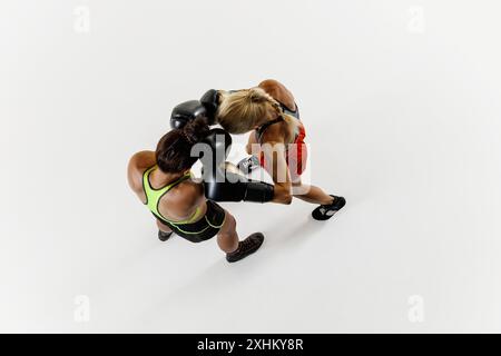 Vista dall'alto di due giovani donne atletiche impegnate in una partita di boxe dinamica, che gareggiano per la vittoria isolata su sfondo bianco Foto Stock