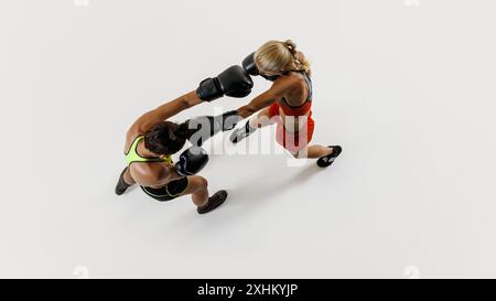 Vista dall'alto di due giovani donne atletiche impegnate in una partita di boxe dinamica, che gareggiano per la vittoria isolata su sfondo bianco Foto Stock