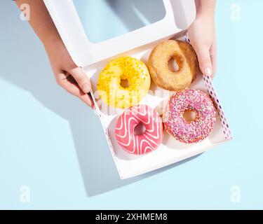 Mani che tengono una scatola di ciambelle su sfondo blu Foto Stock