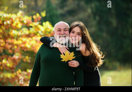 La nipote cresciuta con il nonno anziano lo abbraccia parlando in piedi all'aperto. Figlia adulta che si prende cura di passare il tempo con il vecchio papà. Attenzione ai vecchi Foto Stock