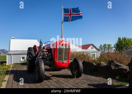 Vecchio trattore agricolo rosso con bandiera nazionale islandese in cima, parcheggiato in un'azienda agricola in Islanda, nessuno. Foto Stock