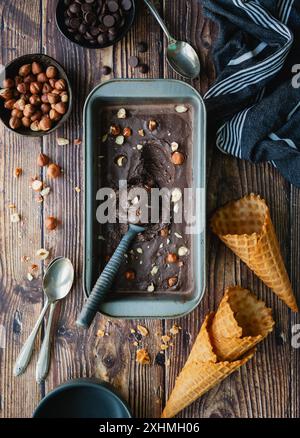 Testa di gelato alle nocciole e coni al cioccolato sul tavolo di legno. Foto Stock