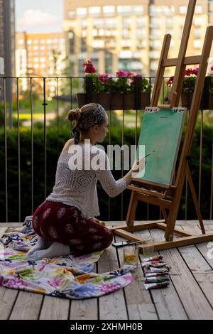 Artista donna dipinge su tela, pitture a olio. Cavalletto in terrazza, in estate. Foto Stock