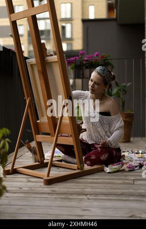 Artista donna dipinge su tela, pitture a olio. Cavalletto in terrazza, in estate. Foto Stock