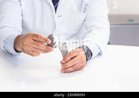 Primo piano delle mani di un chirurgo ortopedico che tiene e mostra una protesi dell'anca. Ideale per temi medici e sanitari. Foto Stock