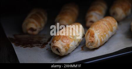 Primo piano di salsicce fatte in casa con impasto su teglia da forno. Involtini di salsiccia appena sfornati. Pranzo e snack deliziosi Foto Stock