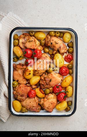 Cosce di pollo cotte con patate novelle, pomodori ciliegini e olive al vino bianco in stile borgognone in rustico piatto da forno e sfondo in legno. Coperchio o ar Foto Stock