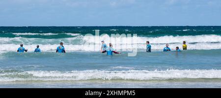 Un'immagine panoramica di un gruppo di vacanzieri che hanno una lezione di surf alla spiaggia di Towan a Newquay, in Cornovaglia nel Regno Unito. Foto Stock