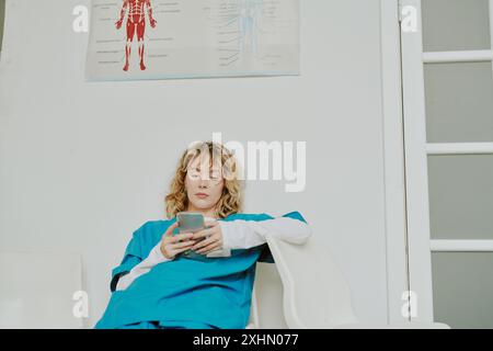 Stanca giovane infermiera caucasica che fa evasioni con l'aiuto di smartphone dopo un lungo turno di notte Foto Stock