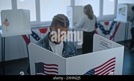 L'uomo afroamericano viene a votare in cabina nell'ufficio del seggio elettorale. Il giorno delle elezioni nazionali negli Stati Uniti. Razze politiche di candidati presidenziali statunitensi. Concetto di patriottismo e dovere civico. Foto Stock