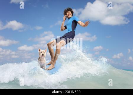 Ritratto a figura intera di un uomo in muta con un cane che cavalca una tavola da surf in mare e utilizza uno smartphone Foto Stock