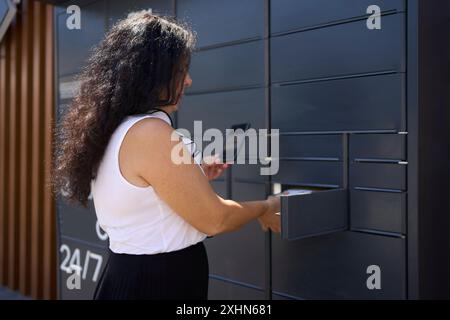 una donna preleva un pacco da un terminale postale utilizzando un'applicazione mobile Foto Stock