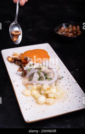 Cucchiaio di mais arrosto su un piatto di ceviche peruviana su sfondo scuro. Foto Stock