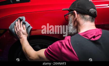 Esperto di autolavaggio che utilizza un panno in microfibra per asciugare una moderna Sportscar rossa. Uomo adulto pulizia della sporcizia, preparazione di una muscle car americana per il dettaglio. Foto cinematografica creativa con veicolo sportivo Foto Stock