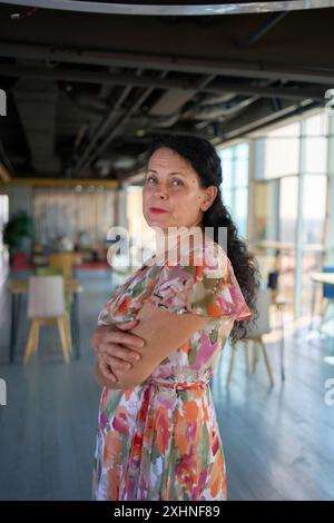 donna d'affari degli anni '60 in abito floreale in un moderno ufficio di coworking Foto Stock