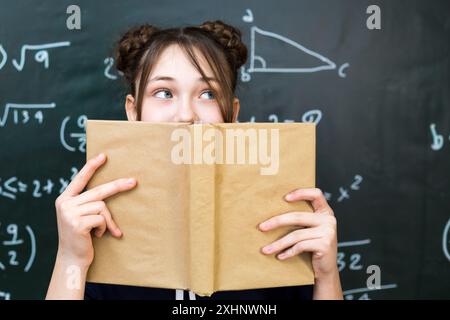 la studentessa ride in classe, coprendosi la bocca con un libro aperto. Foto Stock