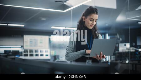 Responsabile del dipartimento di ingegneria del software tecnologico che utilizza un computer portatile. Donna multietnica che guarda a distanza e pensa mentre lavora in ufficio Foto Stock