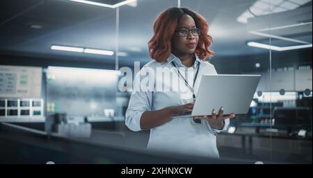Responsabile del dipartimento di ingegneria del software tecnologico che utilizza un computer portatile. Donna nera che guarda in lontananza e pensa mentre lavora in ufficio Foto Stock