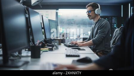 Amministratore di sistema che lavora in una struttura di e-Business di ricerca su un computer desktop. Sviluppatore di software specializzato in abiti casual che indossano cuffie e aggiornano il database del sistema server Foto Stock