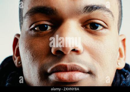 Primo piano di un giovane uomo con capelli corti, carnagione scuro e orecchini in entrambe le orecchie. La sua espressione seria è evidenziata dallo sguardo concentrato del suo Foto Stock