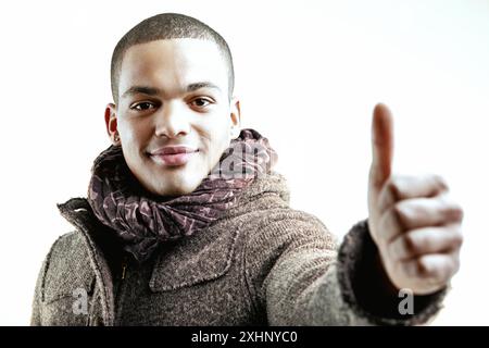 Uomo (in primo piano) con un cappotto grigio e sciarpa blu, sorridente calorosamente e con il pollice in alto (fuori fuoco). Il suo gesto e la sua espressione trasmettono positività, frie Foto Stock