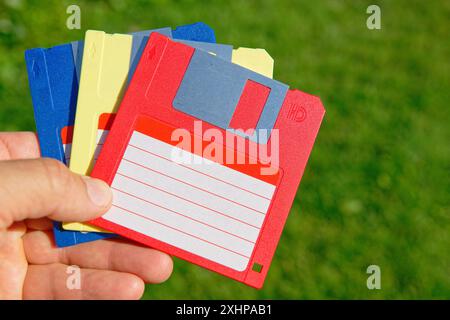 Floppy disk colorati vintage in una mano su prato verde. Vecchie tecnologie Foto Stock