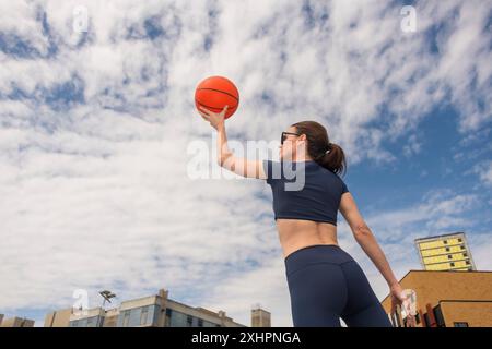 Vista posteriore, donna che tiene in mano un pallacanestro all'aperto, sfondo urbano, scatto, visuale ad angolo basso Foto Stock