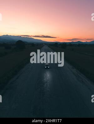 Epico paesaggio di un'auto in una strada abbandonata con un bellissimo e vibrante tramonto sullo sfondo. Foto Stock