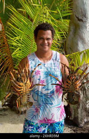 Polinesia francese, isola di Tahaa'a, pescatore che tiene grandi aragoste vive tra le mani su uno sfondo di palme da cocco Foto Stock