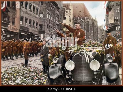 1927 Adolf Hitler in piedi nella sua auto Mercedes aperta al Congresso del Rally di Norimberga 1927 cartolina a colori, con fiori lanciati dagli ammiratori, dando il suo saluto nazista Heil Hitler alla sfilata e passando le truppe Sturmabteilung SA con le loro uniformi marroni con bracciali di svastica. Julius Streicher, un noto e virulento antisemita e proprietario di Der Sturmer, davanti a Hitler con una tuta oscura. 1927 Foto Stock