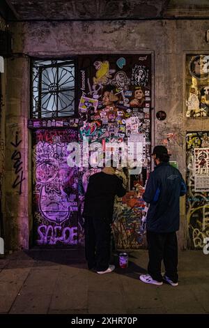 Due persone volano pubblicando poster sul muro dei graffiti a88 in un'immagine artistica di Street art Foto Stock