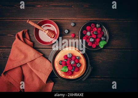 Colazione, pancake con frutti di bosco e miele, vista dall'alto, fatti in casa, niente persone, su uno sfondo di legno Foto Stock