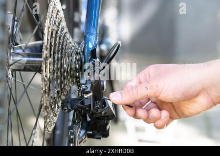 primo piano di un deragliatore posteriore di una bicicletta regolabile con una mano maschile. Il meccanico della bicicletta regola il deragliatore posteriore e ripara la bicicletta in officina. manutenzione biciclette a. Foto Stock