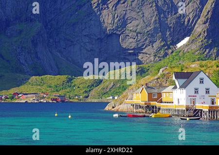 Pittoresca vista dei villaggi costieri norvegesi con il colorato rorbuer accanto al mare cristallino e alle spettacolari montagne sullo sfondo, Sakrisoey Foto Stock