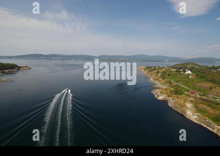 Una barca naviga attraverso il mare calmo lungo una costa verde in una giornata di sole, vista dal ponte RV 17, strada costiera, Norvegia Foto Stock