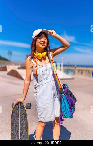 Ritratto verticale di un'adolescente asiatica cinese con il suo skateboard al parco pubblico che si prepara a pattinare Foto Stock