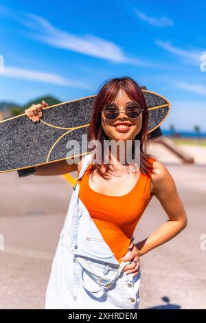 Ritratto verticale di una giovane donna in abiti estivi e occhiali da sole con pattino sulle spalle Foto Stock