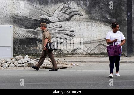 Un uomo cammina davanti a un muro con una grande opera d'arte di mani mentre una donna si rivolge a fianco, Cuba, grandi Antille, Caraibi, America centrale, America Foto Stock