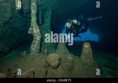 Subacquea tuffatrice femmina tuffatrice che nuota nell'area di ingresso della grotta sottomarina della grotta delle stalattiti sott'acqua con formazioni di stalagmiti a stalattiti Foto Stock