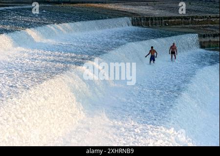 Uomini che si bagnano nello spruzzo delle cascate della Lech weir, acqua bianca schiumosa agitata, fiume Lech, Landsberg am Lech, alta Baviera, Baviera Foto Stock